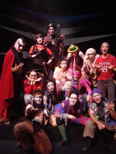 The full company, some twenty performers in monster make-up, costume and street clothes, piled up on a set of black stairs for a group photograph.