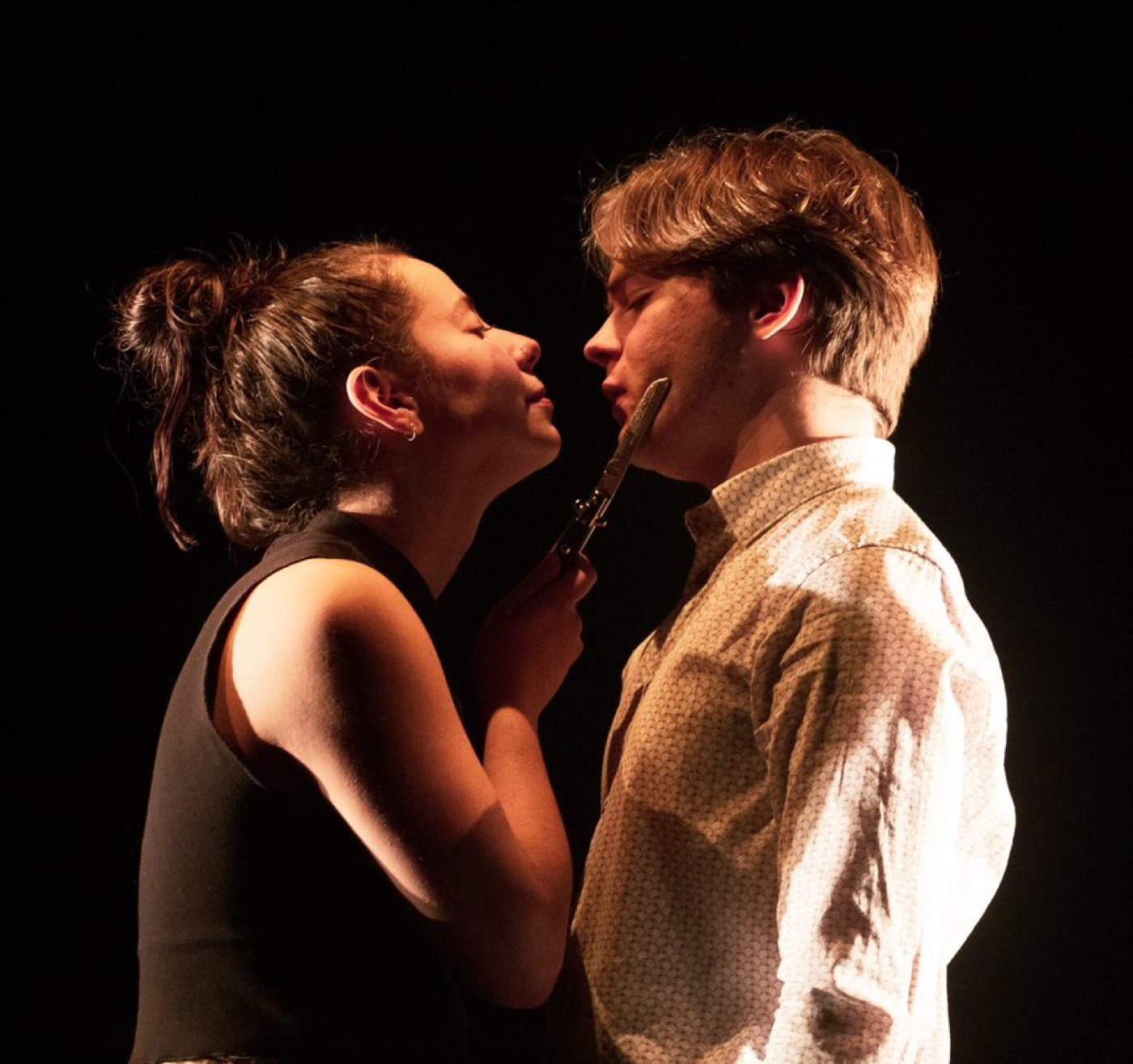 Basil and Delia face to face in tight light, a blade held between them.